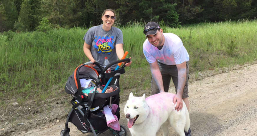 Two people with a stroller and a large white dog, both smudged with colored powder.